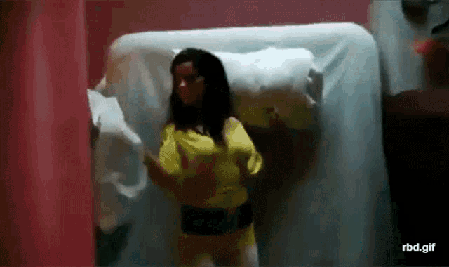 a woman in a yellow shirt is standing in front of a bed in a room .
