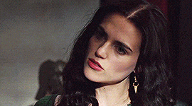 a woman with long dark hair is wearing earrings and a green shirt .