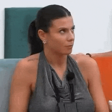 a woman in a gray tank top is sitting on a couch looking at the camera .