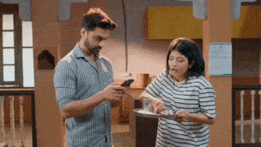 a man is looking at his phone while a woman holds a tray of food .