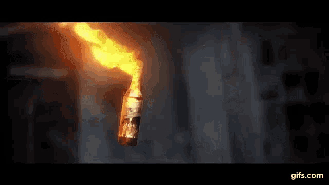 a molotov cocktail is being thrown from a bottle in the dark .
