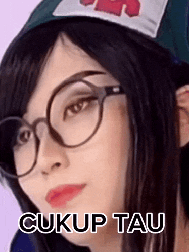 a woman wearing glasses and a hat with the words cukup tau on it .
