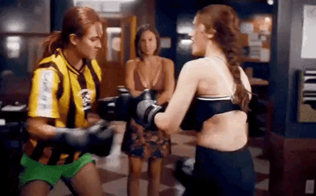 a man and a woman are boxing in a gym while a woman watches .