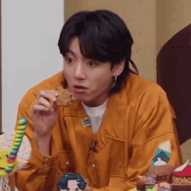 a young man in an orange jacket is eating a cookie while sitting at a table .