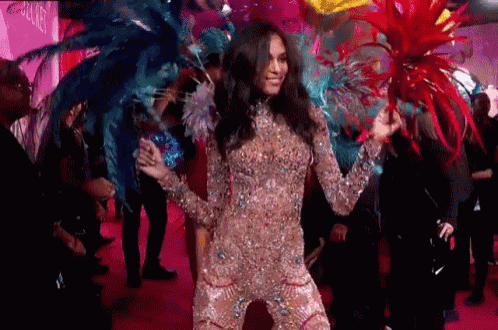a woman in a costume with feathers on her head is dancing on a pink carpet .