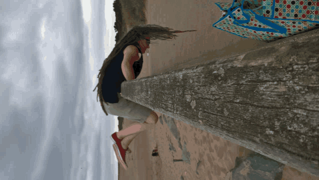 a person with dreadlocks leaning on a wooden post