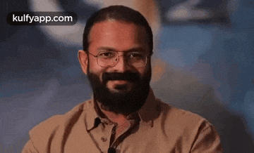 a man with a beard and glasses is sitting down and making a funny face .