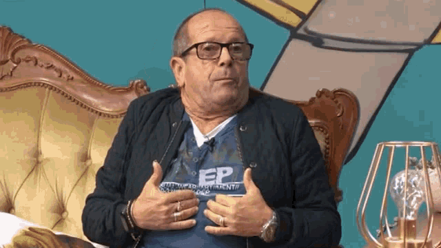 a man wearing glasses and a shirt that says ep is sitting on a couch