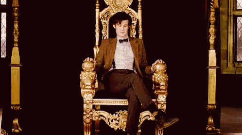 a man in a suit and bow tie is sitting on a throne