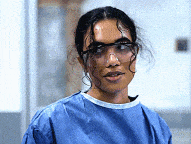 a woman wearing a blue gown and safety goggles looks at the camera .