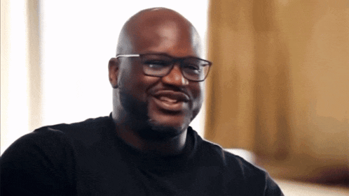 a bald man wearing glasses and a black shirt smiles for the camera