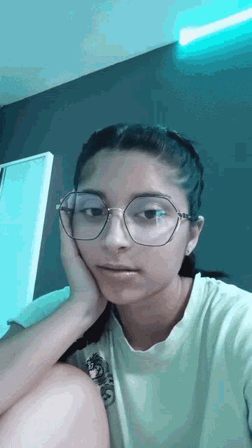 a girl wearing glasses and a yellow shirt is sitting down with her hand on her face
