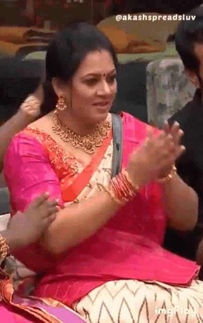 a woman in a pink blouse and a gold necklace is clapping