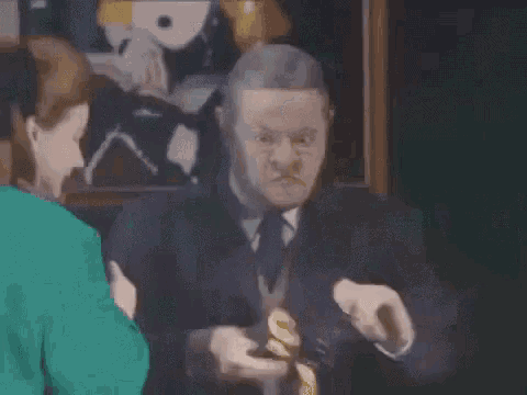 a man with glasses is talking to a woman in front of a painting