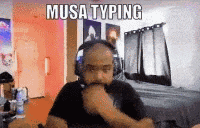 a man wearing headphones is typing on a computer while sitting in a room .