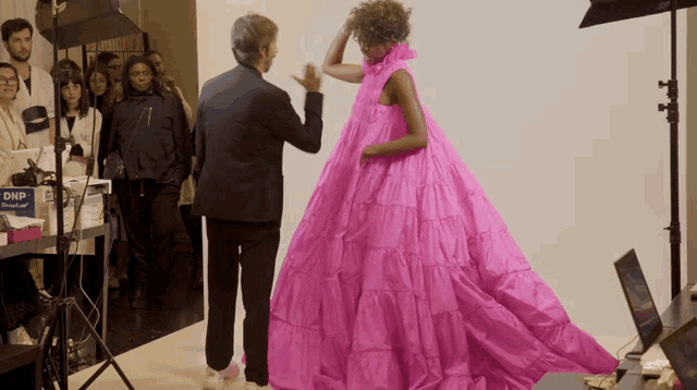 a woman in a bright pink dress is being photographed by a man in a black suit