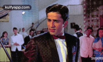 a man in a tuxedo and bow tie is standing in a crowded room .