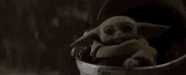 a baby yoda is sitting in a bucket and looking at the camera .