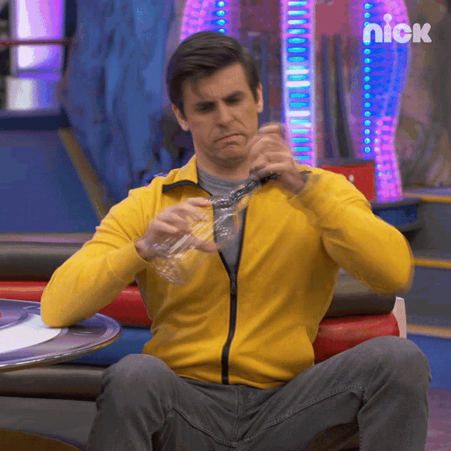 a man in a yellow jacket sits at a table with a nick logo on the bottom
