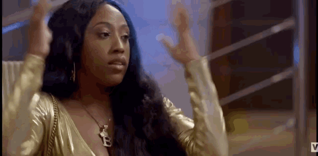 a woman with long black hair is wearing a gold dress and necklace .