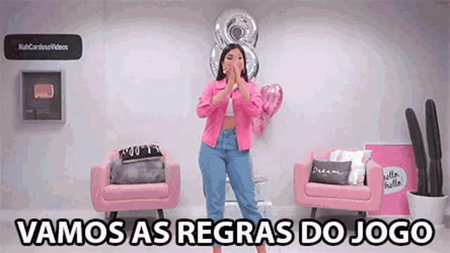 a woman in a pink jacket is standing in front of two pink chairs with the words vamos as regras do jogo below her .