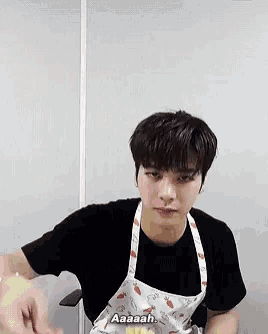 a young man wearing an apron is sitting in a chair and making a funny face .