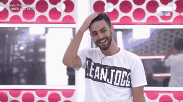 a man with a beard wearing a lean jogs t-shirt is smiling and touching his head .