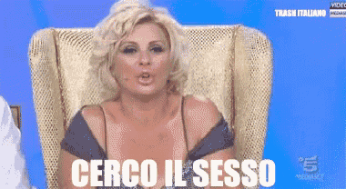 a woman sitting in a chair with the words cerco il sesso written on the screen behind her