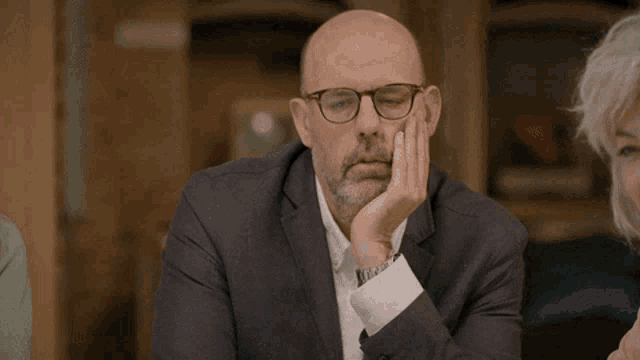 a bald man wearing glasses and a suit is making a funny face