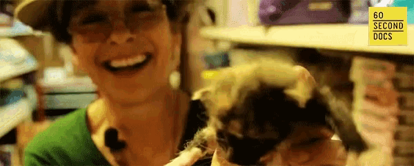 a woman is smiling while holding a kitten in front of a sign that says 60 second docs