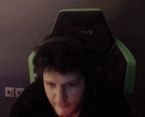a man wearing headphones is sitting in a green gaming chair and making a funny face .