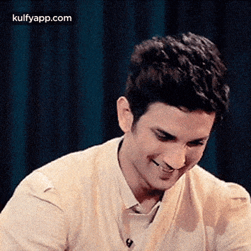 a man is smiling and looking down while wearing a white shirt and a tan sweater .
