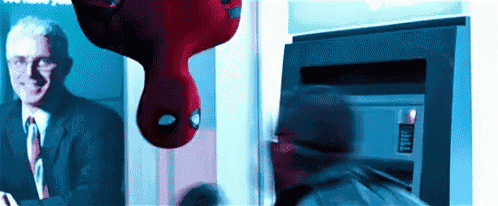 a man in a suit and tie is standing next to a spider man hanging upside down .