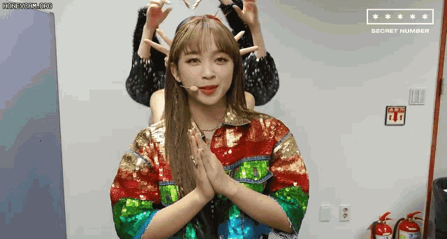 a woman in a colorful jacket is making a heart with her hands .