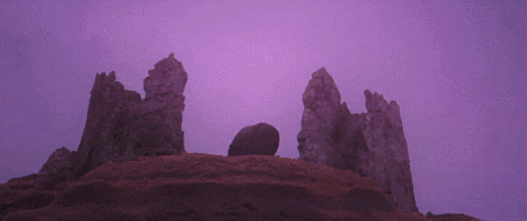 a woman in a white dress is holding a guitar on top of a rocky hillside