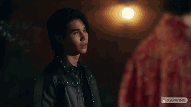 a man in a leather jacket is standing next to another man in a red shirt