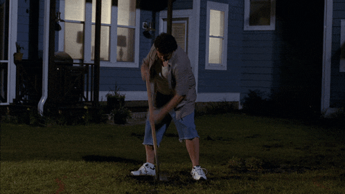 a man standing in front of a house holding a large wooden stick