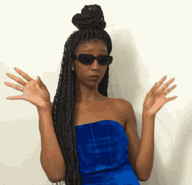 a woman wearing sunglasses and a blue dress has her hands up in the air