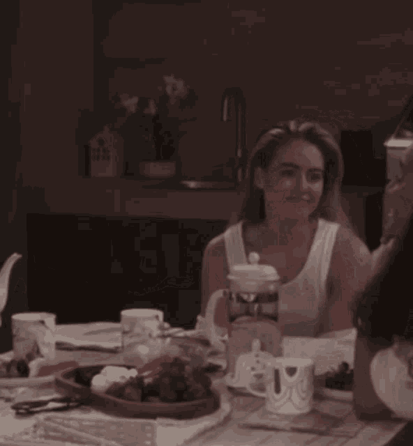 a woman in a white tank top sits at a table with a pitcher that says ' i love you ' on it