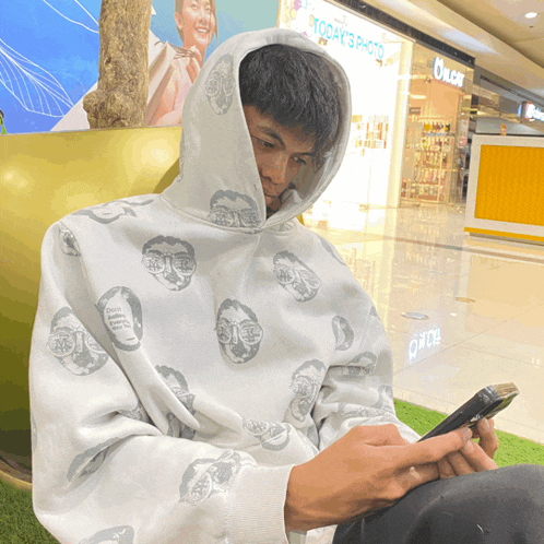 a man wearing a white hoodie is looking at his phone in front of a store called today 's photo