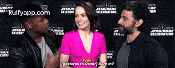 a woman in a pink dress is talking to two men in front of a star wars celebration backdrop