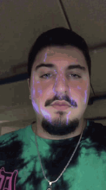 a man with a beard wearing a green tie dye shirt and a necklace