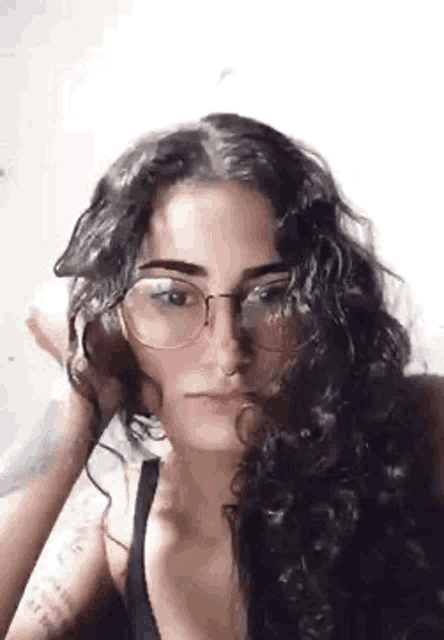 a woman with curly hair and glasses is holding her hair in her hand .