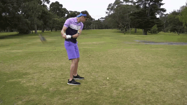 a man in purple shorts and a blue headband is swinging a golf club