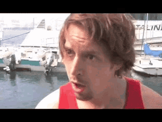 a man in a red tank top stands in front of boats with a sign behind him that says tallinn