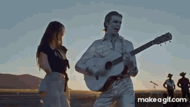 a man and a woman are standing next to each other while a man plays a guitar .