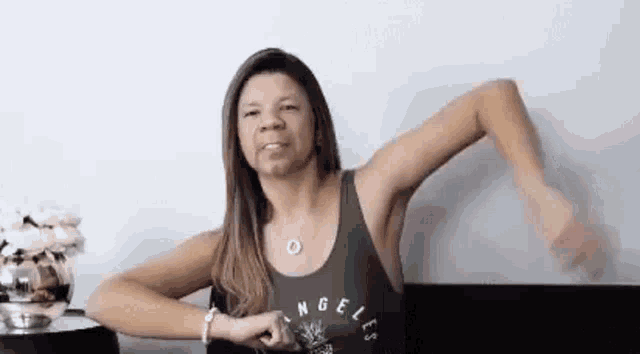 a woman in a green tank top is sitting at a table with her arms outstretched .
