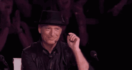 a man in a hat and tie is pointing at the camera while sitting in front of a microphone .