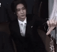 a young man in a suit and tie is sitting in a chair holding a sword .