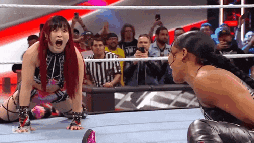 a woman is kneeling down in a wrestling ring while another woman looks on .
